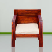 A wooden single seater sofa with a beige cushion, placed against a neutral background.