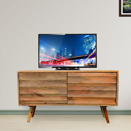 A natural finish mango wood TV cabinet with 2 doors, mounted on a floor, with a flat-screen TV placed on top of it.