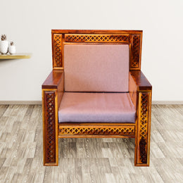 A single seater sofa made of Sheesham wood with a cushion cover, in Kapasi brown color, placed on a grey floor with a white wall in the background.