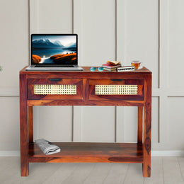 Wooden desk with a laptop, books, and a plant in a room with a light gray wall.