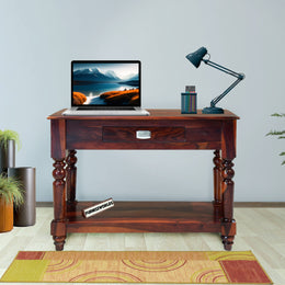 Wooden desk with laptop, lamp, and decor items in a room with light blue walls and wooden floor.