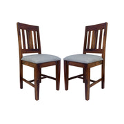 A pair of wooden dining chairs with a teak finish and padded seats in a room setting.