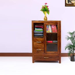 A brown finish solid wood standard bookcase with drawers, containing books and folded garments, with a vase of flowers on top.