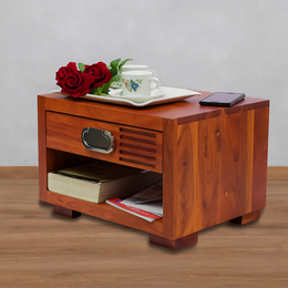 Wooden side table with a drawer, books, a teacup, and phone on top against a gray background.