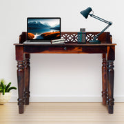 Wooden desk with laptop, lamp, and decorative items against a white wall.