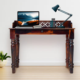 Wooden desk with laptop, lamp, and decorative items against a white wall.