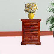 A solid wood bedside table with drawers in a maple finish, displayed in a room setting with a vase of flowers on top.