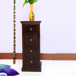 A brown mango wood bedside table with four drawers, placed against a white background with a yellow vase on top and a colorful stick to the side.