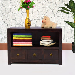 A brown wooden chest of drawers with three drawers, placed against a wall with a decorative vase on top and some books and a teddy bear arranged on the drawers.