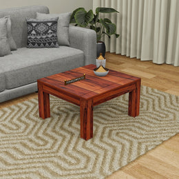 A solid wood coffee table in Kapasi brown finish placed on a zigzag pattern rug, with a grey sofa and a decorative item on the table.