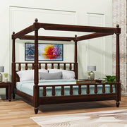 A wooden queen size poster bed with a honey finish, featuring a four-poster design and placed in a bedroom setting with bedding and pillows.