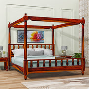A wooden queen size poster bed with a honey finish, featuring a four-poster design and placed in a bedroom setting with bedding and pillows.