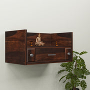 A wooden wall-mounted temple with a drawer, featuring a Buddha statue and LED lights, mounted on a wall beside a green plant.