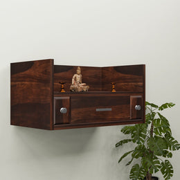A wooden wall-mounted temple with a drawer, featuring a Buddha statue and LED lights, mounted on a wall beside a green plant.