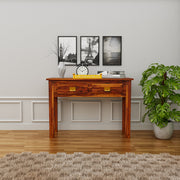 Wooden desk in a room with framed pictures on the wall and a plant.