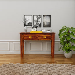 Wooden desk in a room with framed pictures on the wall and a plant.