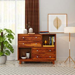 Wooden dresser with decorative items in a room with a plant and lamp.