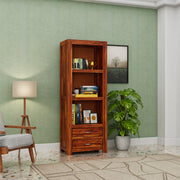 Wooden bookshelf with books and decor items against a green wall with a lamp and plant.