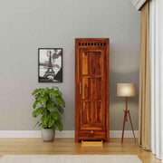 Wooden wardrobe in a room with a plant, lamp, and framed picture on the wall.