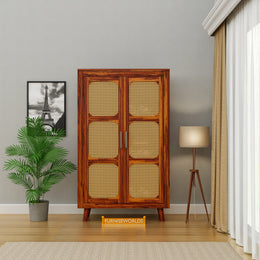 Wooden cabinet with wicker doors in a room with a plant, lamp, and framed picture.