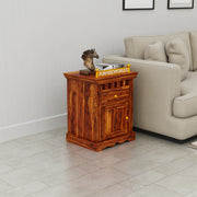 Wooden side table with a drawer in a living room setting, featuring a beige sofa and a small statue.
