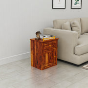 Wooden side table in a living room with a beige sofa and framed pictures on the wall.