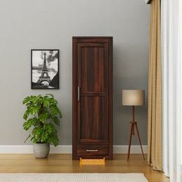 Wooden wardrobe in a room with a plant, lamp, and framed picture on the wall.