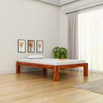 Wooden bed frame with mattress in a room with light-colored walls and wooden floor.