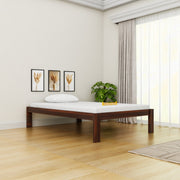 Wooden bed frame in a room with light-colored walls, a plant, and framed pictures.