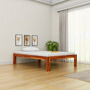 Wooden bed frame in a room with light-colored walls, a plant, and framed pictures.