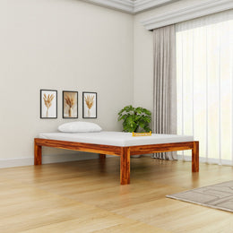Wooden bed frame in a room with light-colored walls, a plant, and framed pictures.