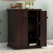 A wooden bar cabinet in walnut finish with doors, placed in a living room setting, with decorative items on top and glasses inside.