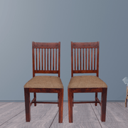 Two wooden chairs with woven seats against a gray wall.