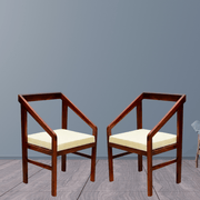 Two wooden chairs with cream cushions on a gray floor and wall.