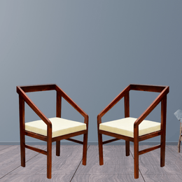 Two wooden chairs with cream cushions on a gray floor and wall.