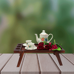 Tea set with teapot and cups on a wooden tray with flowers against a blurred green background