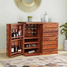 A solid sheesham wood bar cabinet with a honey finish, featuring glass doors, storage for bottles and glasses, and drawers.