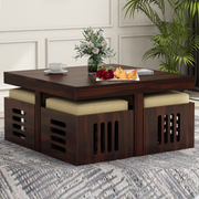 A brown wooden coffee table with four cushioned stools underneath, placed on a patterned rug.