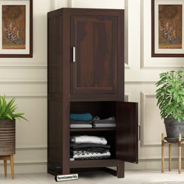 A wooden wardrobe in walnut finish with an open door showing neatly folded clothes inside, placed in a room with decorative wall paintings.