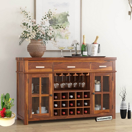 A solid wood bar cabinet with wine storage rack in a honey finish, placed in a living room setting with decorative items on top and around it.