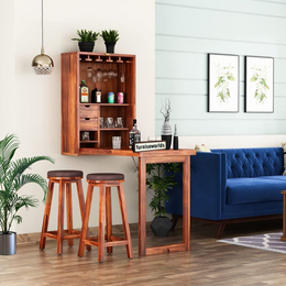 A solid wood bar cabinet with two stools in a teak finish placed in a room with a blue sofa and green plants.