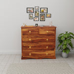 Wooden dresser with decorative items in a room with a plant and wall art.