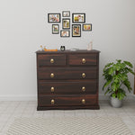 Wooden dresser with gold knobs in a room with a plant and wall art.